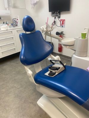 un fauteuil bleu dans le cabinet du dentiste, avec une télévision accrochée au mur