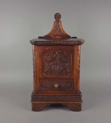 une vieille armoire en bois dont le dessus est sculpté, sur fond gris