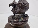 une statue en bronze représentant un oiseau perché sur une table en verre