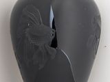 a black vase with a bird on it on a shelf
