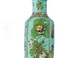a green vase with flowers on it sitting on a stand