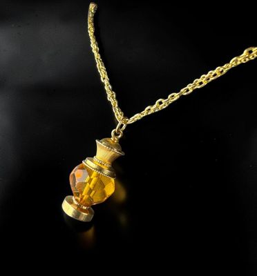 a yellow glass bottle with a gold chain on a black background