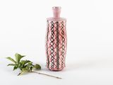 un vase rose posé à côté d'une plante verte sur une surface blanche