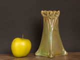 a green vase next to an apple on a table