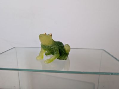 une figurine de grenouille verte posée sur une table en verre