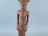 une statue en bois représentant un homme dont le visage et les mains sont posés sur sa poitrine