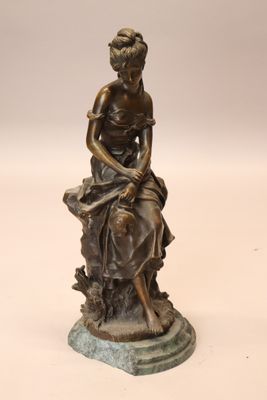 bronze statue of a woman sitting on a rock with a dog