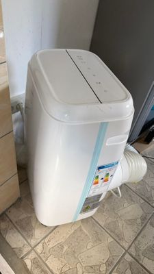 un climatiseur blanc posé par terre à côté d'un réfrigérateur