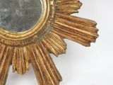 a gold starburst shaped mirror on a white wall