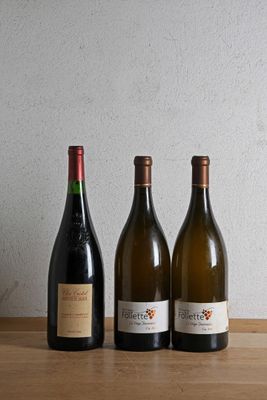 three bottles of wine sit on a wooden table next to a bottle of wine
