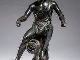 une statue en bronze représentant un homme tenant un ballon de basket-ball, posée sur un socle en marbre