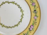 a yellow plate with purple flowers on it on a white table