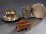 une tasse et une soucoupe en argent posées sur une table, à côté d'une assiette en argent