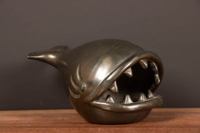 un petit requin en métal, la gueule grande ouverte, posé sur une table en bois
