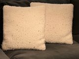two white pillows sitting on top of a black couch next to each other