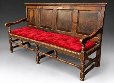 un banc en bois surmonté d'un coussin rouge, sur fond gris
