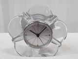 une horloge en verre transparent avec un cadran argenté, posée sur une table blanche