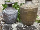 two vases sitting on top of a rock in front of a stone wall