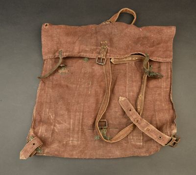 an old brown canvas bag with two straps on a gray surface
