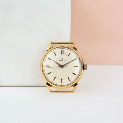 une photo d'une montre en or posée sur une table blanche