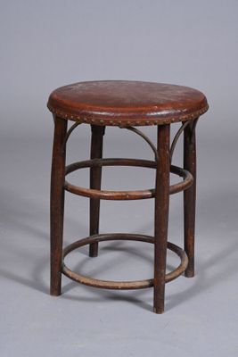 un vieux tabouret en bois avec une assise en cuir, sur fond gris