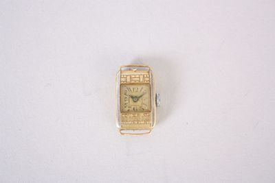 une petite montre-bracelet en or posée sur une surface blanche