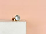 une image représentant une bague en or sertie d'une topaze bleue, posée sur un bloc de marbre