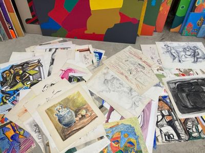 a pile of art work sitting on the floor next to a pile of books