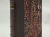 un livre marron à la couverture rouge et noire posé sur une surface blanche