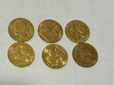 six gold sovereigns, one of which is a sovereign, are on a white surface
