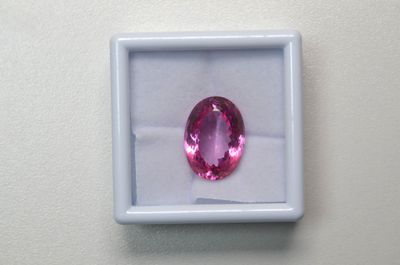 un saphir rose de taille ovale, présenté dans un écrin blanc posé sur un fond blanc
