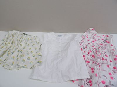Trois vêtements pour bébé sont alignés sur une table blanche