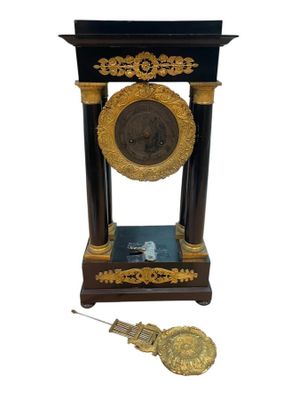 une horloge noire et dorée, surmontée d'un médaillon doré