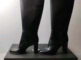 black leather high heel boots on a black box with a white background