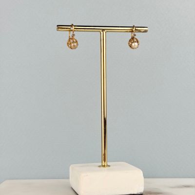 une paire de boucles d'oreilles plaquées or posées sur un socle en marbre