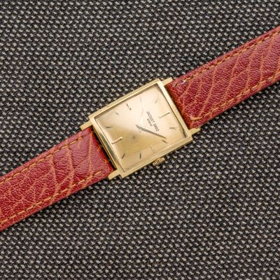 un gros plan d'une montre posée sur une surface noire, avec un bracelet rouge