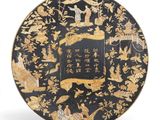 une image représentant une assiette noire et dorée ornée d'oiseaux et de fleurs