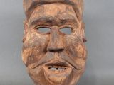 un gros plan d'un masque en bois représentant un visage, posé sur un socle