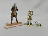 une figurine représentant un homme debout à côté d'un mouton et un homme coiffé d'un chapeau