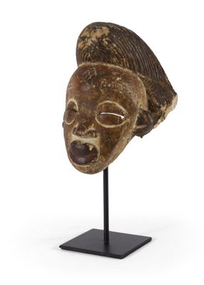 un masque africain posé sur un socle noir, sur fond blanc