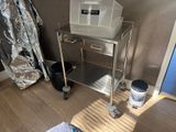 a metal cart with a bin on it in the corner of a room