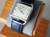 a silver watch on a wooden stand with a black strap
