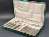un coffret vert ouvert contenant de l'argenterie, posé sur une surface grise