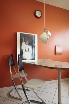 une table et des chaises dans une pièce où est accrochée une horloge au mur