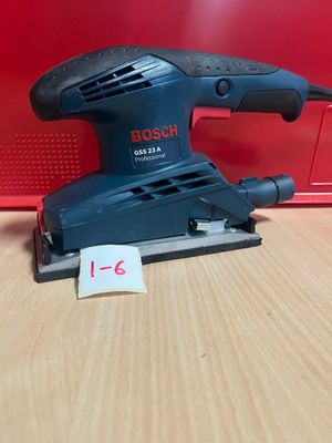 une ponceuse orbitale Bosch posée sur une table, à côté d'une boîte rouge