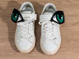 pair of white sneakers with green eyes on them sitting on a wooden floor