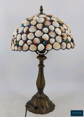 une lampe de table ornée de coquillages, dont le cordon est branché sur le socle
