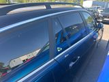 une voiture bleue garée sur un parking, avec une planche de surf posée sur le toit