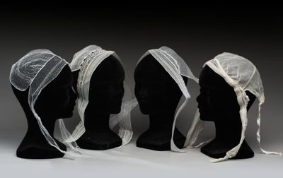 trois têtes de mannequin recouvertes de voiles blancs et une tête de mannequin noire recouverte d'un voile blanc