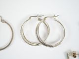three pairs of silver hoop earrings on a white surface
